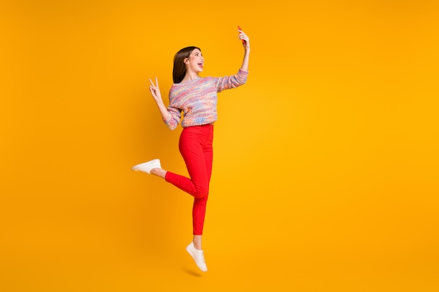 Foto em tamanho grande garota engraçada relaxe férias de outono tire selfie smartphone faça v-sinais videochamada blogueiros influenciadores usam calças vermelhas calças calça sapatos isolados brilhante cor amarela brilhante
