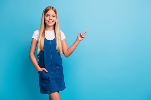Foto em tamanho real de menina de cabelo loiro adolescente fofo positivo ponto espaço vazio usar vestido jeans isolado em fundo de cor azul pastel