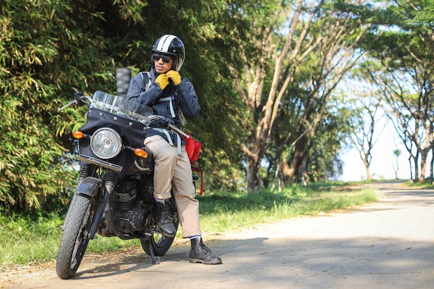 Foto em tamanho real de um homem sentado em uma motocicleta usando óculos de sol e uma jaqueta preta