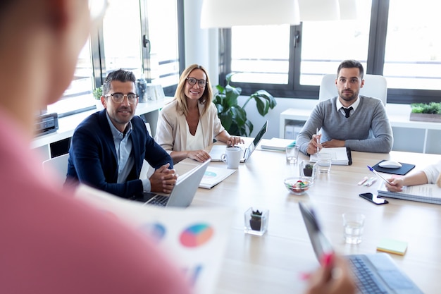 Foto de empresarios tomando notas con el portátil y prestando atención en la conferencia sobre el lugar de coworking.