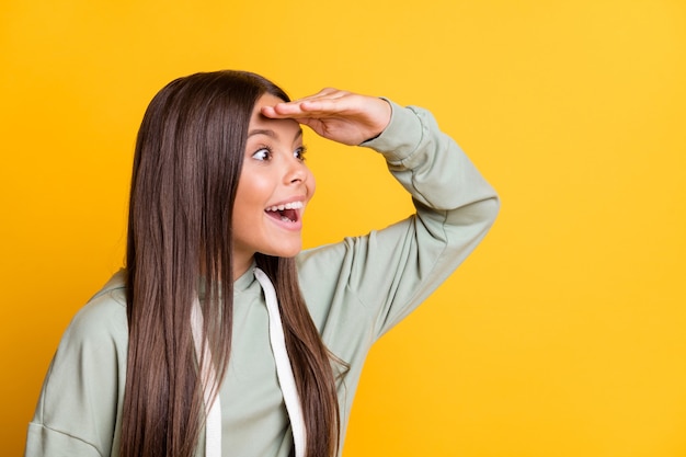 Foto de encantador niño adorable niña vestida con traje verde casual mirando lejos espacio vacío frente brazo aislado fondo de color amarillo