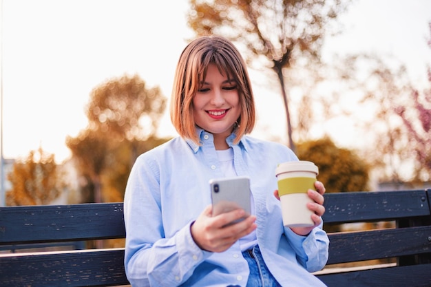 Foto de una encantadora y bonita dama que se comunica con un moderno banco para sentarse sonriendo afuera