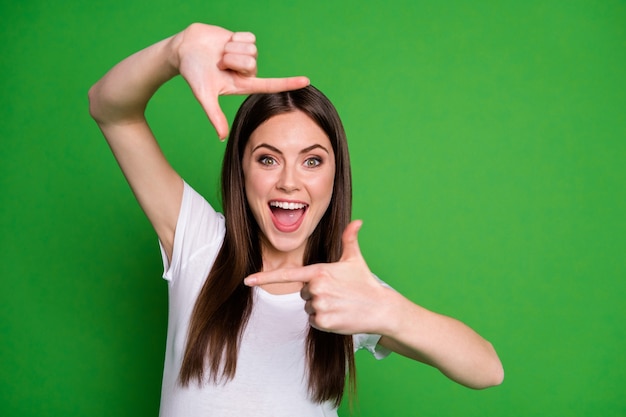 Foto de encantadora chica enérgica usar camiseta blanca haciendo foto dedos boca abierta fondo de color verde aislado