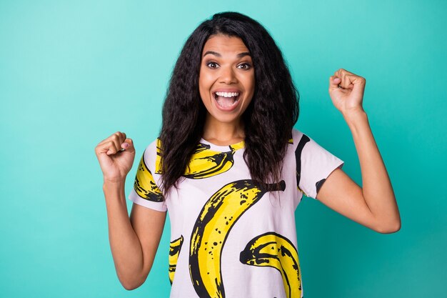 Foto de la encantadora joven negra levantar los brazos con la boca abierta llevar camiseta con estampado de plátano aislado de fondo de color verde azulado
