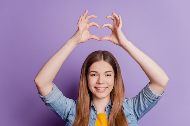 Foto de encantadora niña cariñosa haciendo signo de corazón levantar las manos sobre fondo violeta