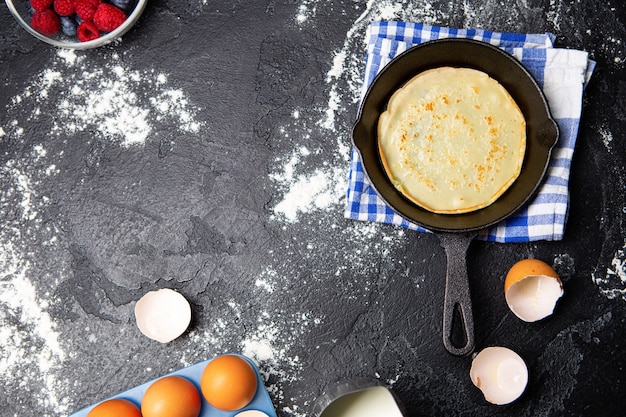 Foto encima de huevos, leche, bayas, pan con panqueques, toallas sobre mesa negra. Ingredientes para panqueques