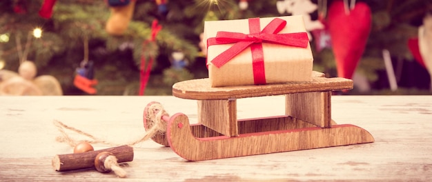 Foto de época Regalo con cinta en trineo de madera para Navidad en el fondo del árbol de Navidad con decoración