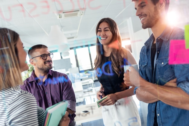 Foto de equipo de negocios exitoso discutiendo juntos frente a tablero de vidrio de oficina en el espacio de coworking.