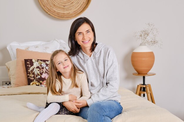 Foto de estilo de vida de madre e hija sentada en la cama en casa