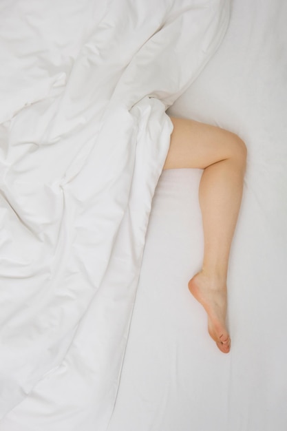 Foto de estilo de vida de una mujer debajo de la manta en la cama, su pierna sobresale