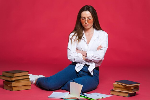 Foto de una estudiante decepcionada usando libros de ejercicios mientras se sienta en el suelo