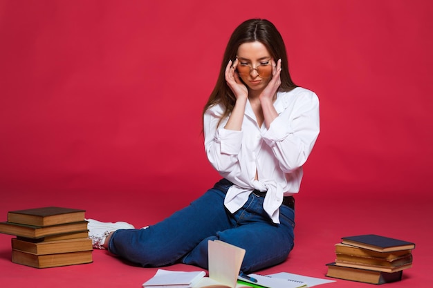 Foto de una estudiante decepcionada usando libros de ejercicios mientras se sienta en el suelo