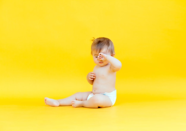 Foto de estudio de un bebé en un pañal. bebé feliz de 10 meses sentado sobre un fondo amarillo.