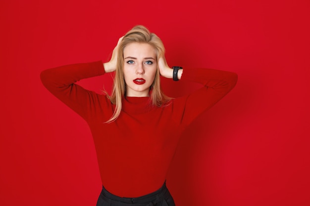 Una foto de estudio de una chica blone de pelo largo lleva una camiseta roja casual. Mujer sosteniendo su cabeza interior