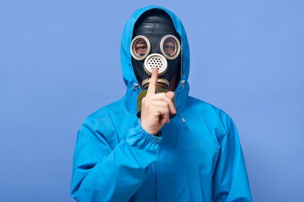 Foto de estudio de científico vistiendo uniforme y máscara de gas, posando aislado sobre azul