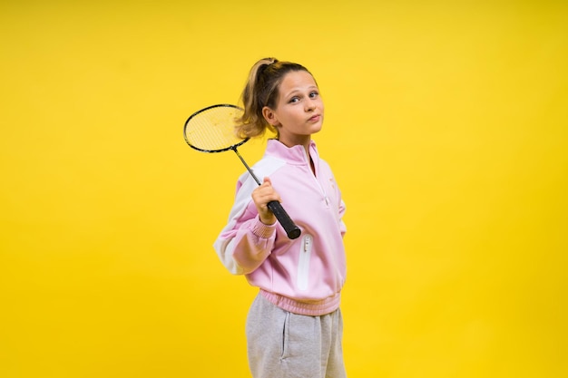 Foto de estudio de cuerpo entero de una niña de diez años sosteniendo una raqueta de bádminton y aislada en amarillo