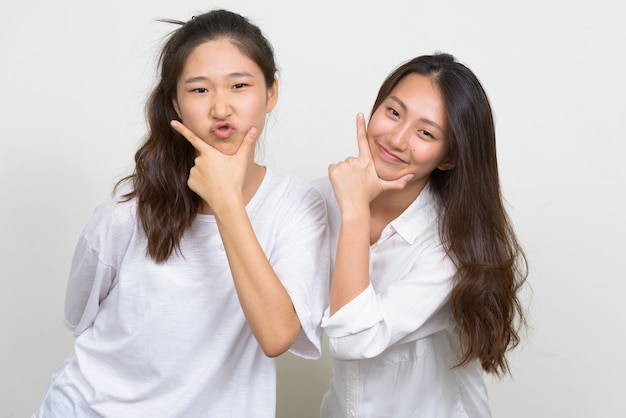 Foto de estudio de dos jóvenes hermosas mujeres coreanas como amigos juntos contra el fondo blanco.