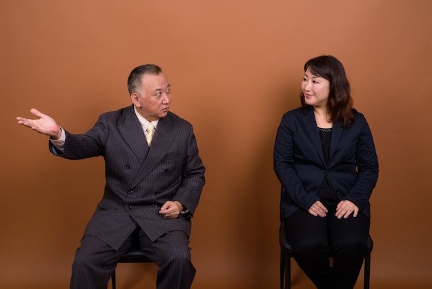 Foto de estudio del empresario japonés maduro y la empresaria japonesa madura juntos contra el fondo marrón