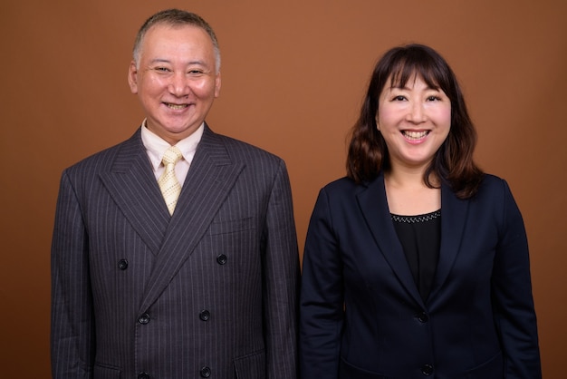 Foto de estudio del empresario japonés maduro y la empresaria japonesa madura juntos contra el fondo marrón