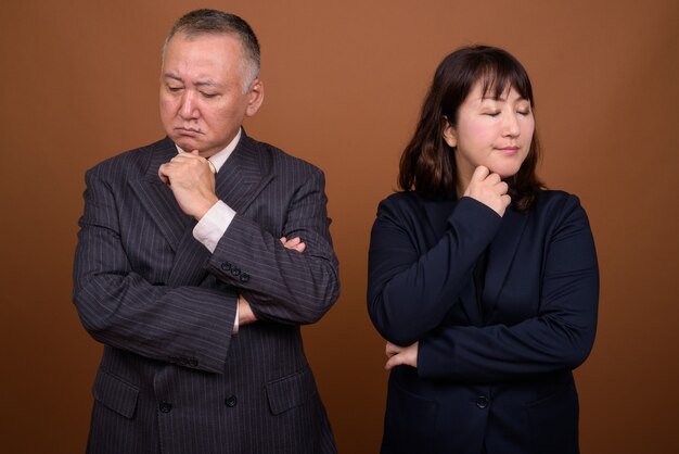 Foto de estudio del empresario japonés maduro y la empresaria japonesa madura juntos contra el fondo marrón