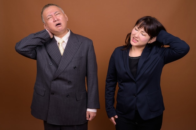 Foto de estudio del empresario japonés maduro y la empresaria japonesa madura juntos contra el fondo marrón