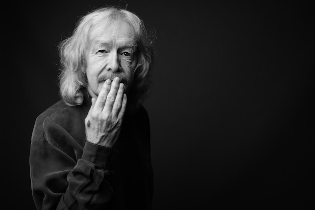 Foto de estudio del empresario senior con bigote contra la pared gris