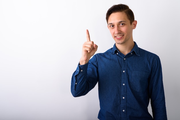 Foto de estudio de feliz apuesto joven sonriendo mientras apunta f