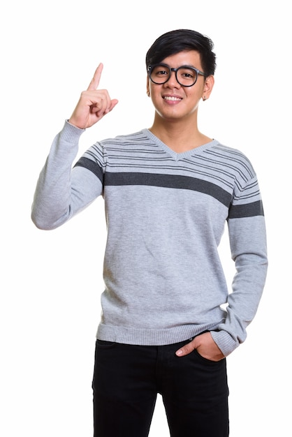 Foto de estudio de feliz hombre asiático sonriendo y apuntando con el dedo hacia arriba