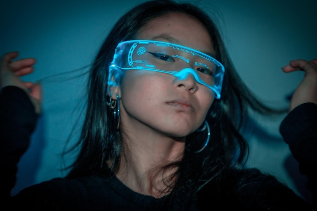 Foto de estudio con fondo azul con luces de neón de una mujer china fresca usando gafas inteligentes futuristas