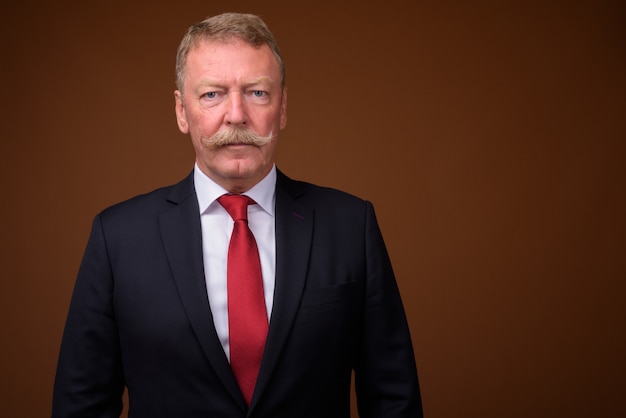 Foto de estudio de guapo empresario senior con bigote contra marrón