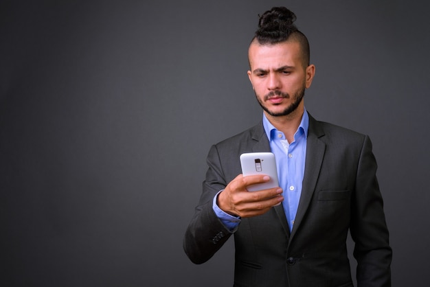 Foto de estudio de guapo empresario turco mediante teléfono móvil contra un fondo gris
