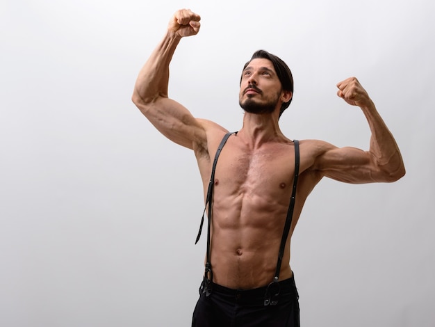 Foto de estudio de guapo flexionando ambos brazos mientras mira hacia arriba s