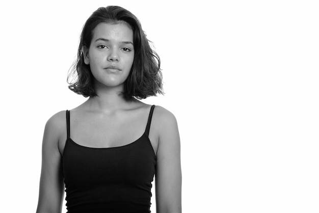 Foto de estudio de hermosa joven adolescente multiétnica con pelo corto aislado sobre fondo blanco en blanco y negro