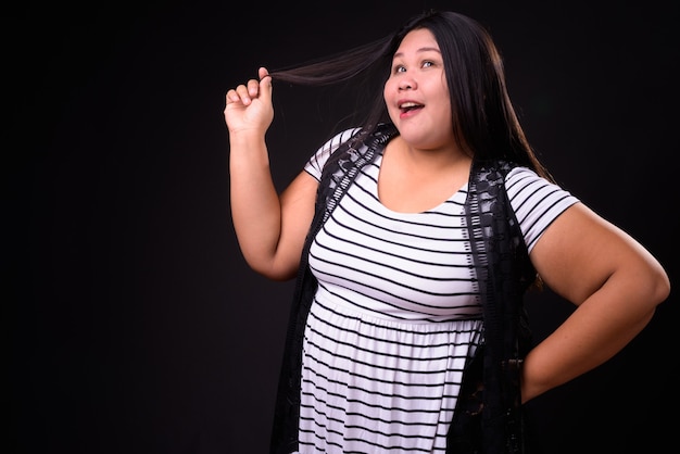 Foto de estudio de hermosa mujer asiática con sobrepeso contra fondo negro