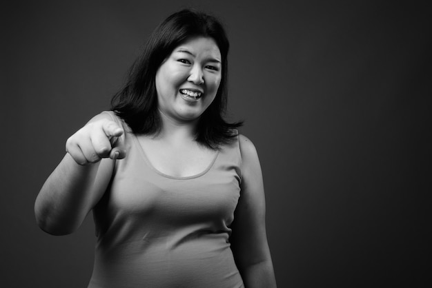 Foto de estudio de hermosa mujer asiática con sobrepeso vistiendo un vestido sin mangas contra un fondo gris en blanco y negro