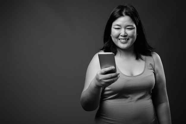 Foto de estudio de hermosa mujer asiática con sobrepeso vistiendo un vestido sin mangas contra un fondo gris en blanco y negro