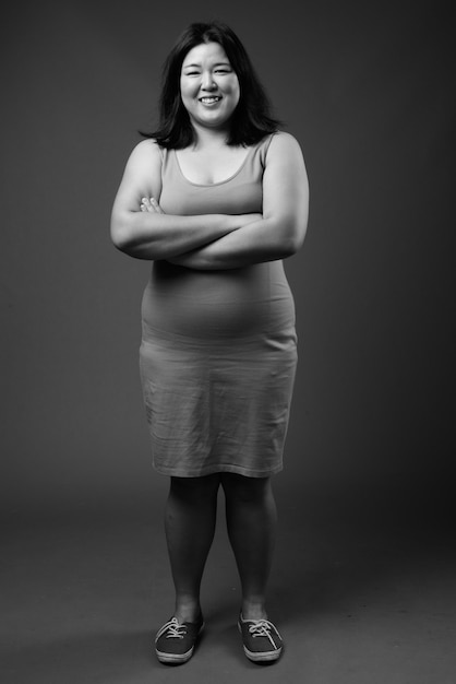 Foto de estudio de hermosa mujer asiática con sobrepeso vistiendo un vestido sin mangas contra un fondo gris en blanco y negro