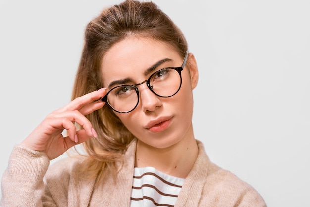 Una foto de estudio de una hermosa mujer pensativa con cola de caballo mira a un lado a través de anteojos y piensa en algo aislado sobre fondo blanco