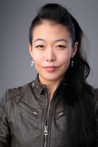 Foto foto de estudio de hermosa mujer rebelde asiática vistiendo chaqueta de cuero contra el fondo gris