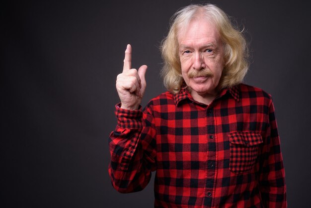 Foto de estudio de hombre mayor con bigote vistiendo camisa a cuadros roja contra un fondo gris