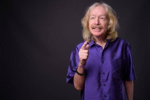 Foto de estudio de un hombre mayor con bigote vistiendo camisa sedosa púrpura contra un fondo gris