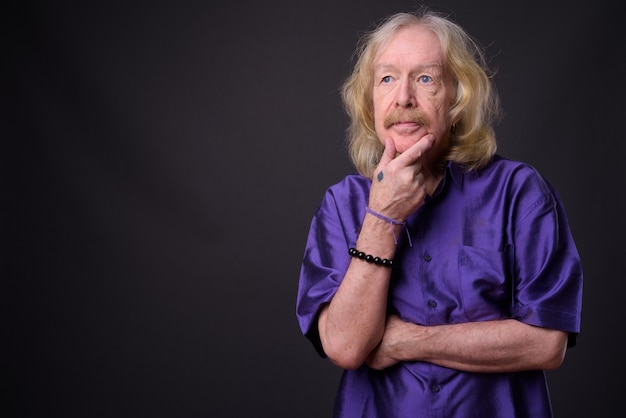 Foto de estudio de un hombre mayor con bigote vistiendo camisa sedosa púrpura contra un fondo gris