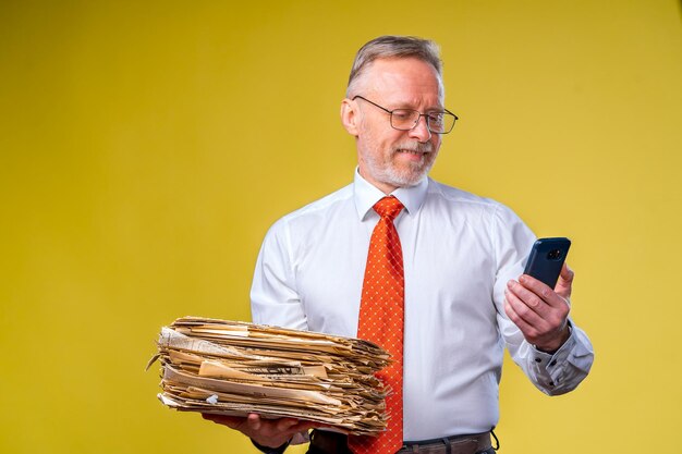 Foto de estudio de un hombre de negocios senior mirando el teléfono sosteniendo un montón de papeles Fondo amarillo