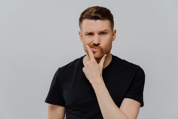 Una foto de estudio de un hombre serio y descontento sostiene que los labios de los bolsos de la barbilla se ven con una expresión pensativa poners en algo que trata de decidirse vestido con ropa informal aislada sobre un fondo azul