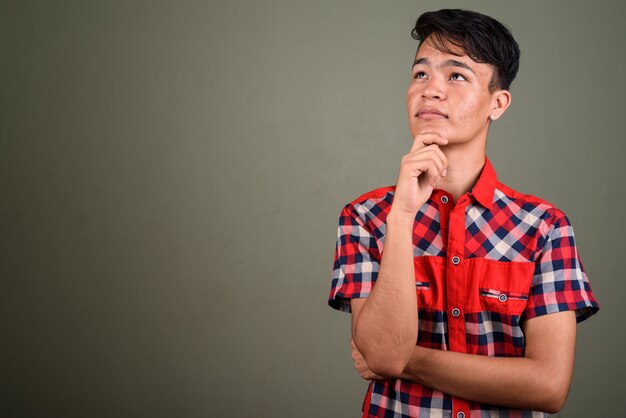 Foto de estudio de un joven adolescente vestido con camisa roja a cuadros contra colores