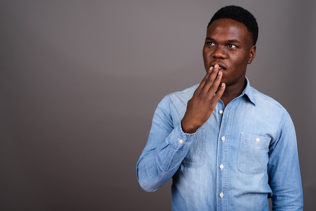 Foto de estudio de joven africano vistiendo camisa de mezclilla contra un fondo gris