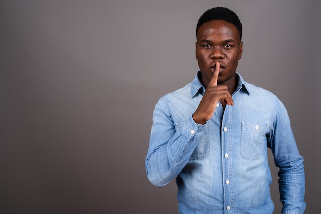 Foto de estudio de joven africano vistiendo camisa de mezclilla contra un fondo gris