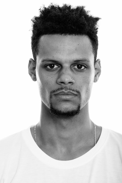 Foto de estudio de joven apuesto hombre africano barbudo con cabello afro aislado sobre fondo blanco en blanco y negro