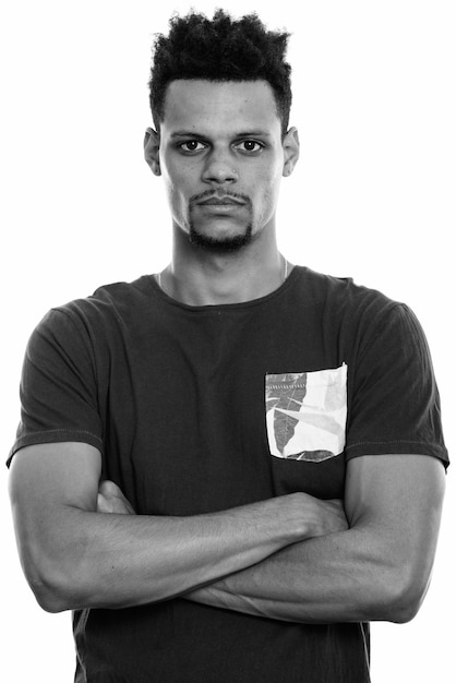 Foto de estudio de joven apuesto hombre africano barbudo con cabello afro aislado sobre fondo blanco en blanco y negro