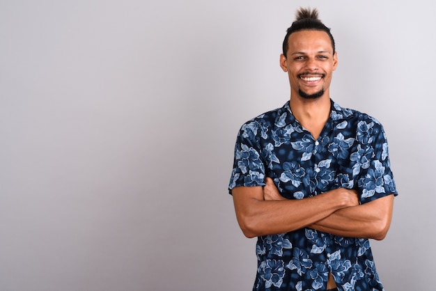 Foto de estudio de joven apuesto hombre africano barbudo vistiendo camisa hawaiana con el pelo atado contra un fondo gris